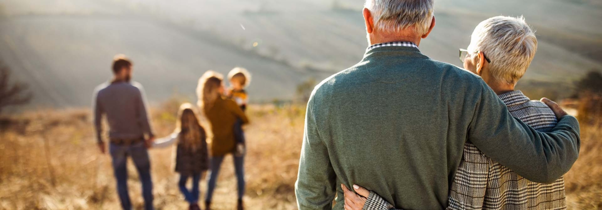 Rear view of embraced senior couple looking at their family in nature.